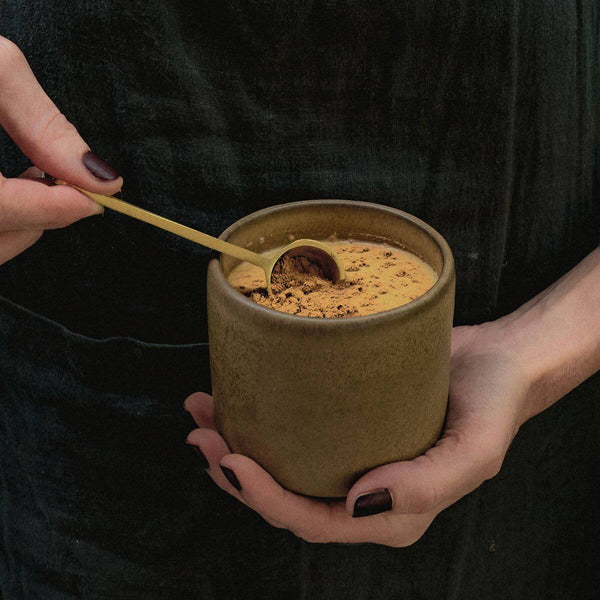 Hands holding a cup of warm hot chocolate with a brass spoon